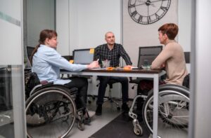 a man discussing something with two women in wheelchairs in the office
