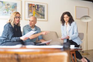 Two women and a man sitting on a couch in an office space with documents in their hands