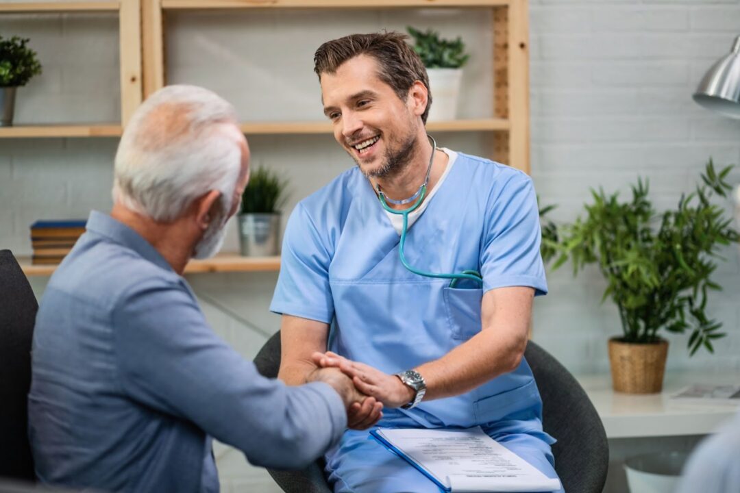 Happy doctor speaking to senior man while shaking hands with him