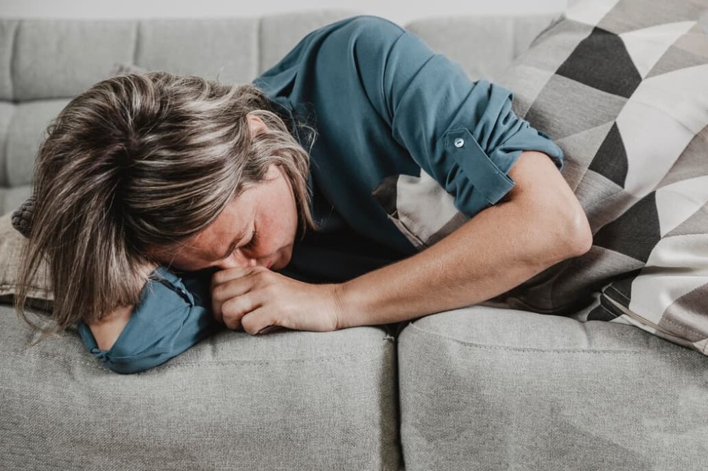 A woman overwhelmed with emotion lies on a couch, hugging a pillow