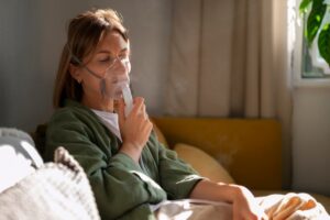 Woman sitting on the couch, using a nebulizer.