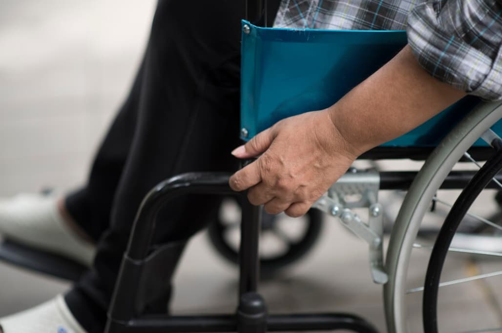Close-up of a person's hand on the wheel of a wheelchair, holding a blue folder